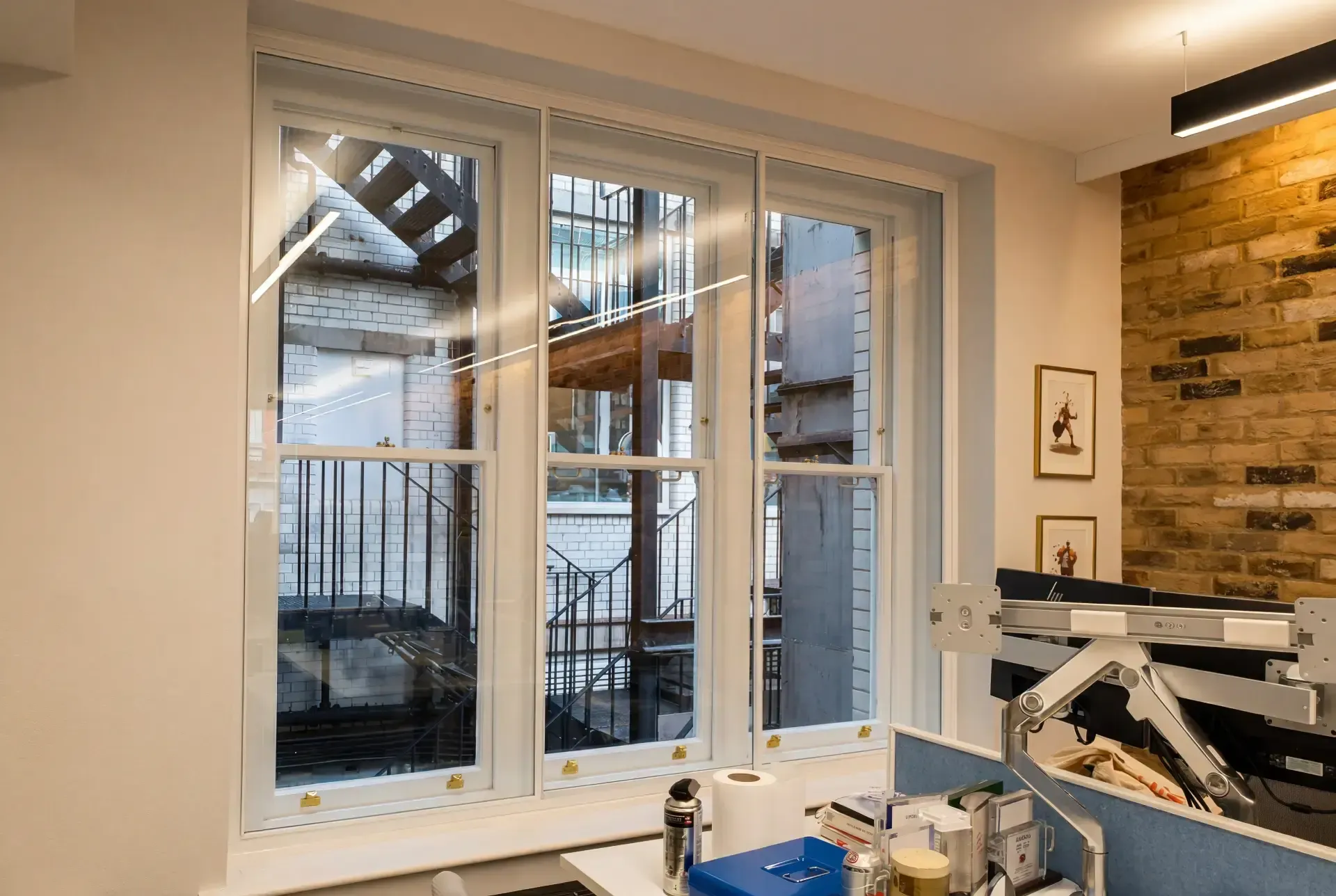 Office workspace with secondary glazing on a three-pane sash window facing a light well and brick wall