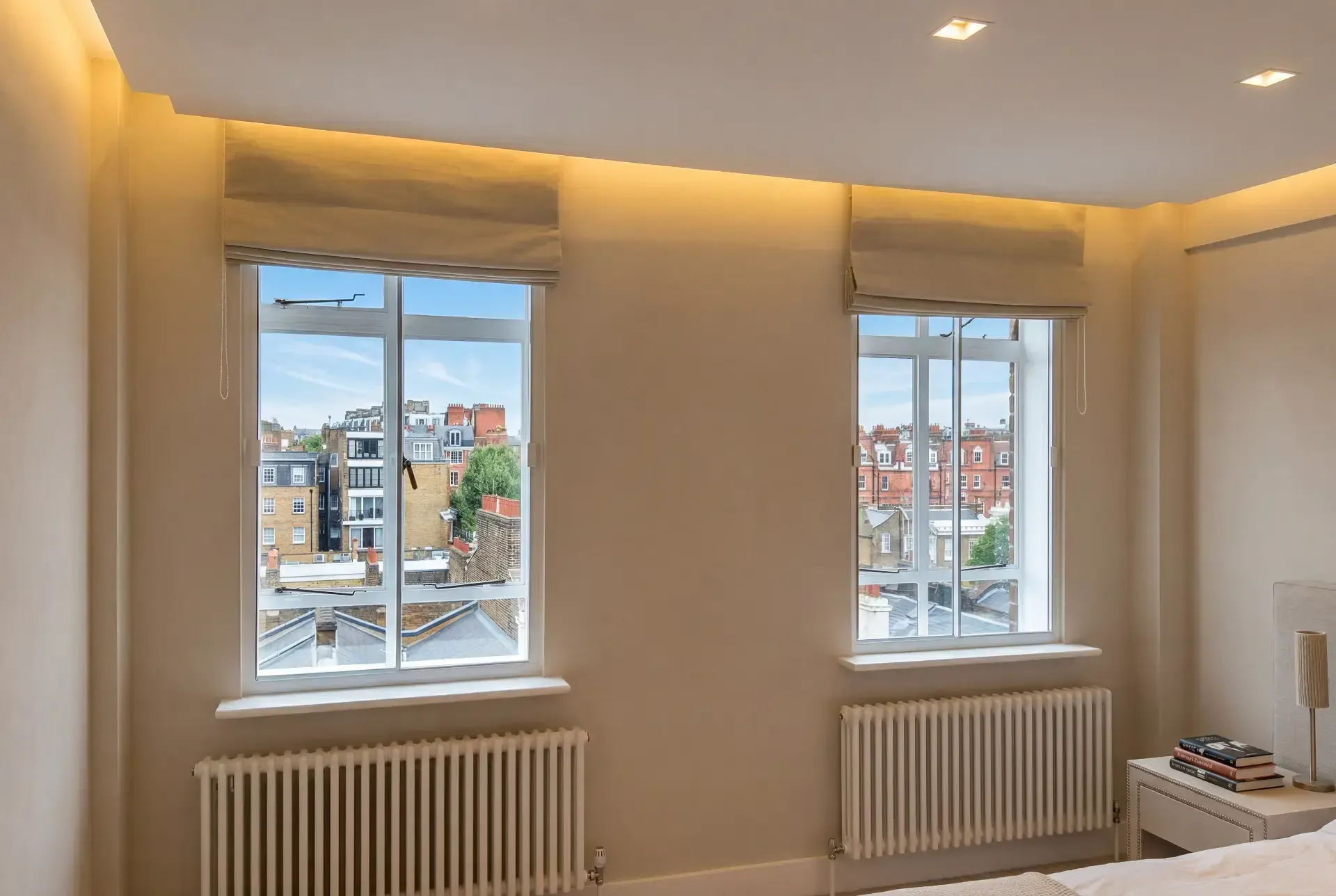 Bedroom with two windows fitted with acoustic secondary glazing behind Roman blinds, rooftop views over London