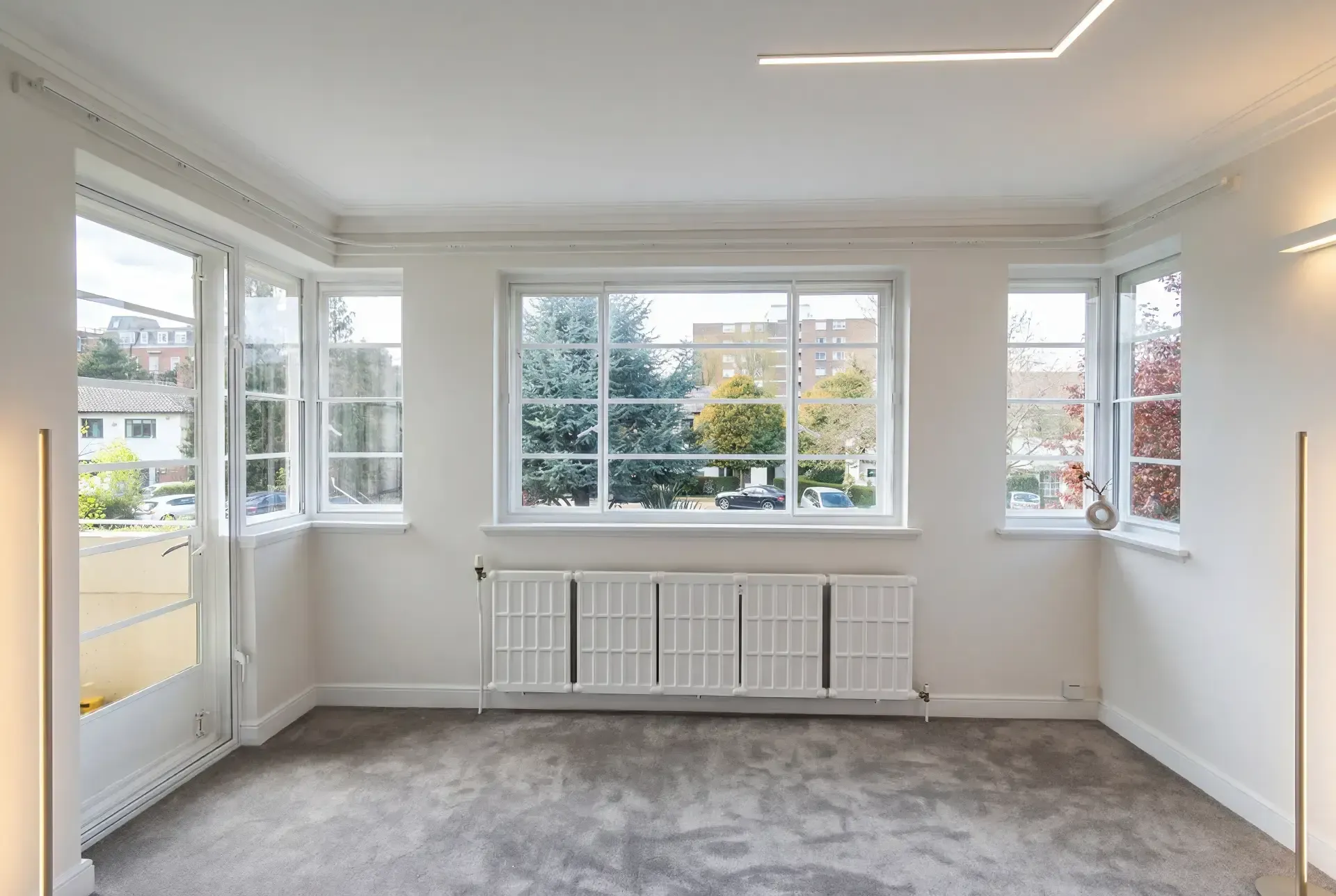 Bright empty reception room with secondary glazing across a wide picture window and balcony door