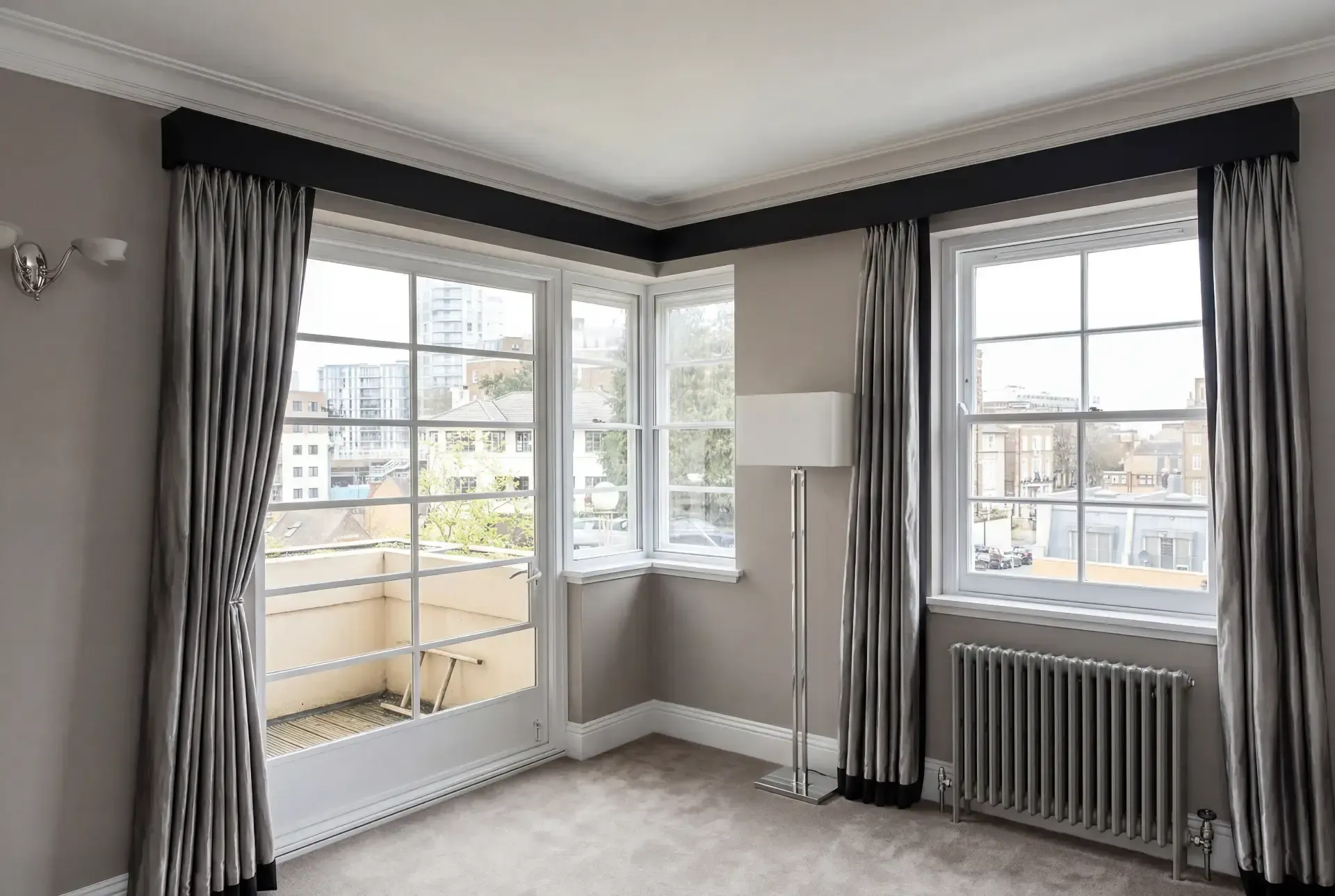Corner living room with secondary glazing on a bay window and balcony door, dressed with curtains and pelmets