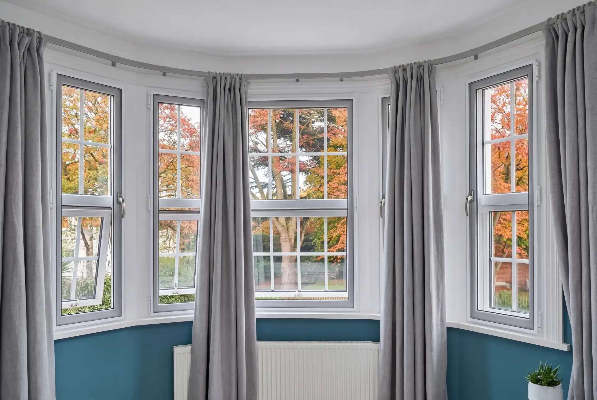Curved bay of casement windows in a 1930s home fitted with secondary glazing behind full-length curtains