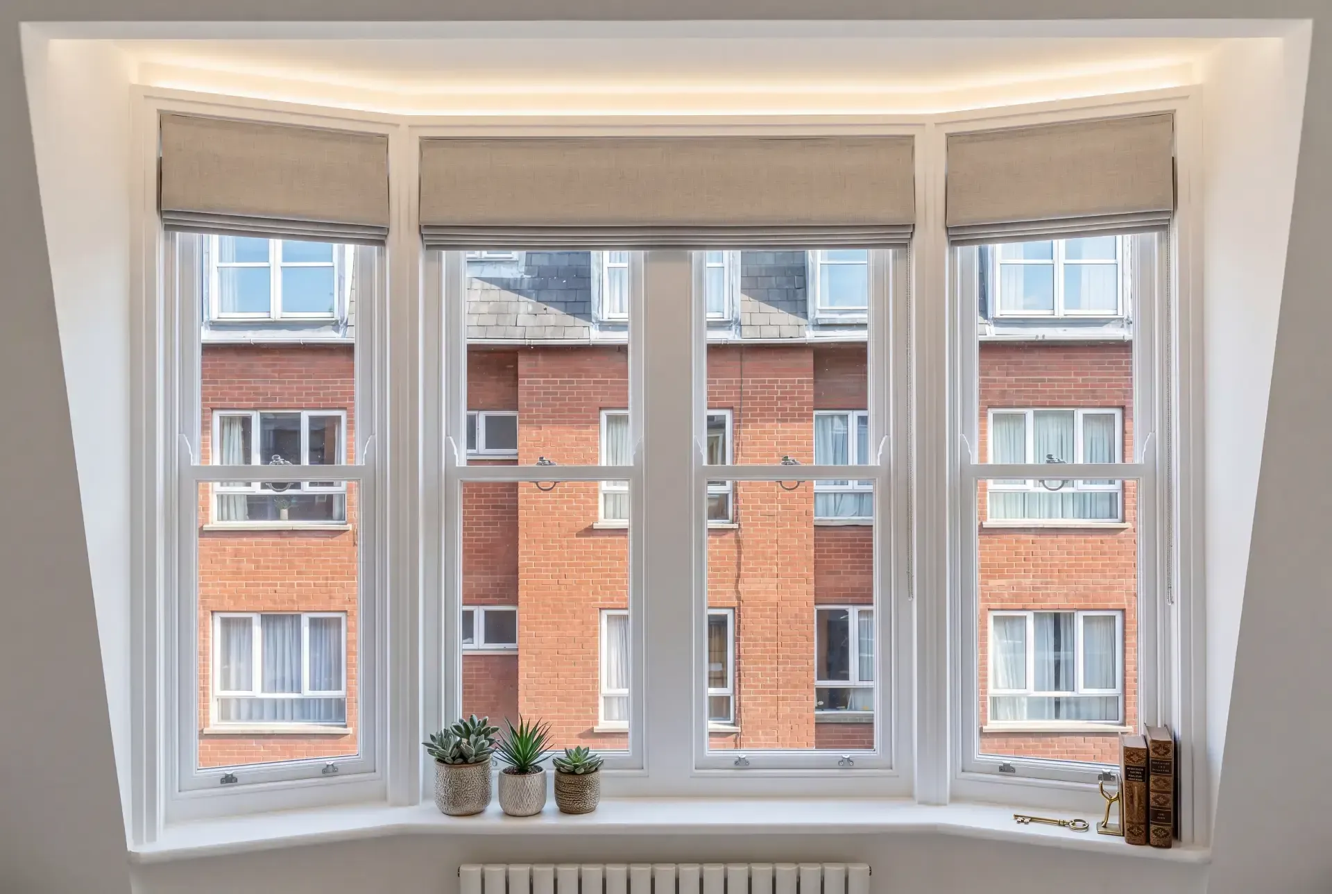 Splayed bay of four sash windows fitted with secondary glazing beneath linen Roman blinds
