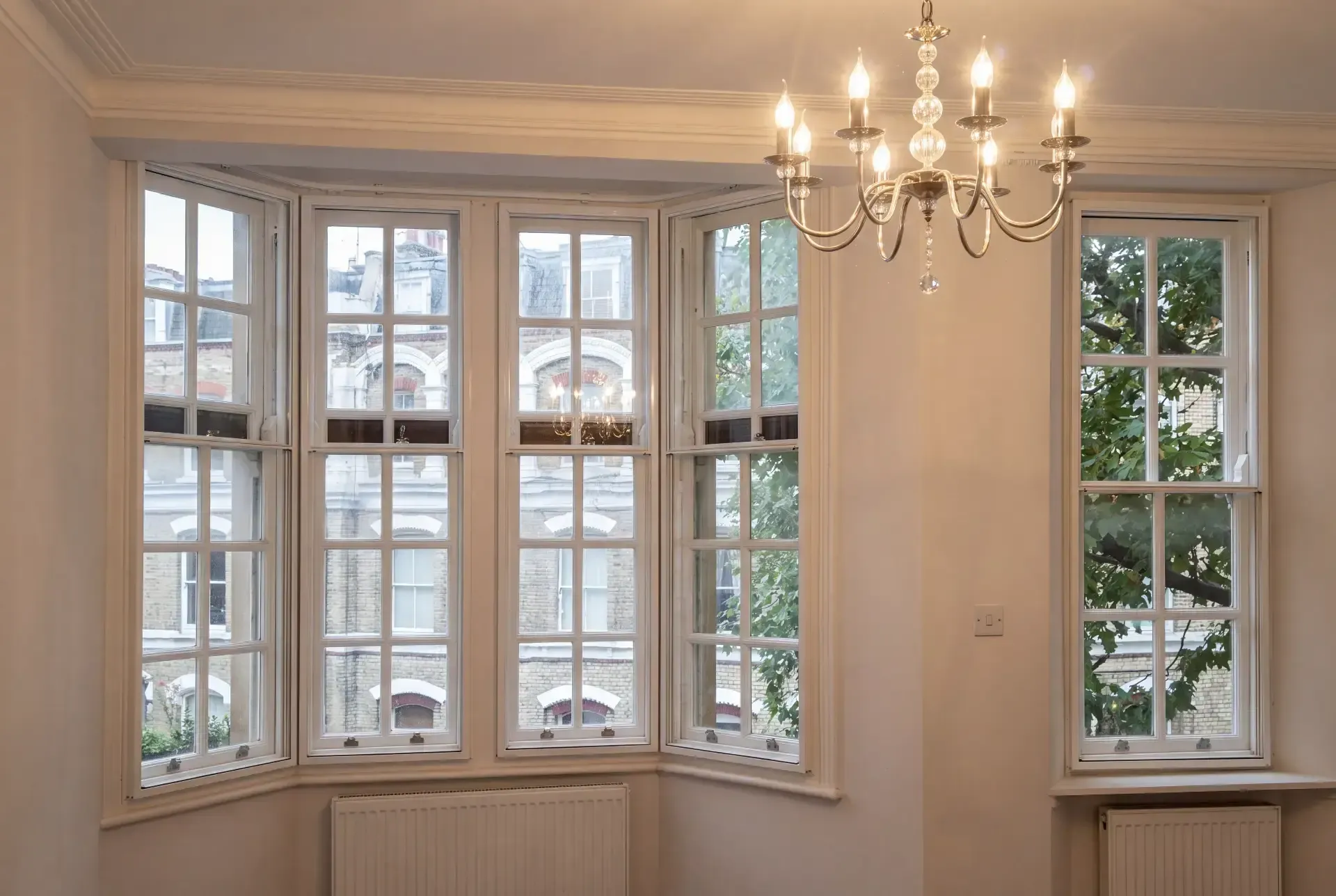 Splayed Victorian bay of georgian-bar sash windows fitted with secondary glazing in a chandelier-lit London reception room