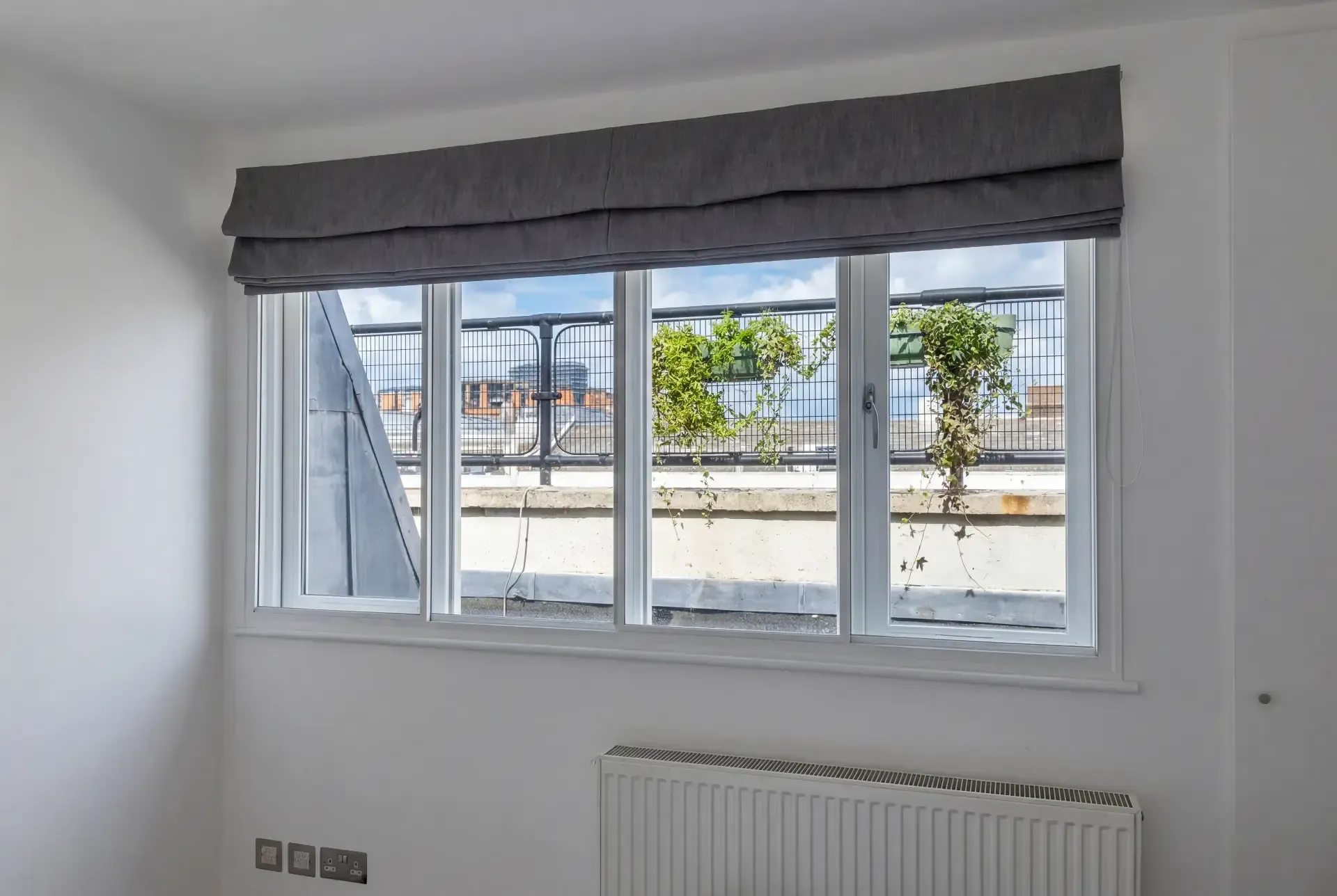 Wide four-pane window with secondary glazing and grey Roman blind in a converted top-floor room