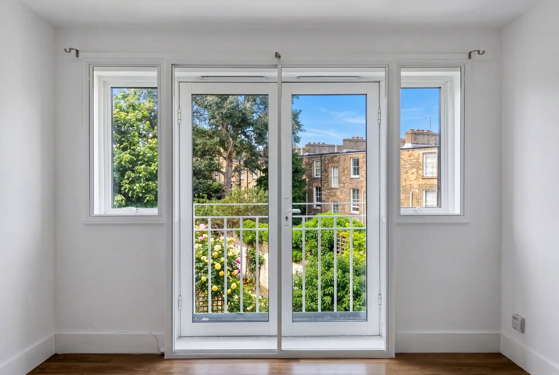 Balcony doors flanked by two casement windows fitted with secondary glazing overlooking a London garden