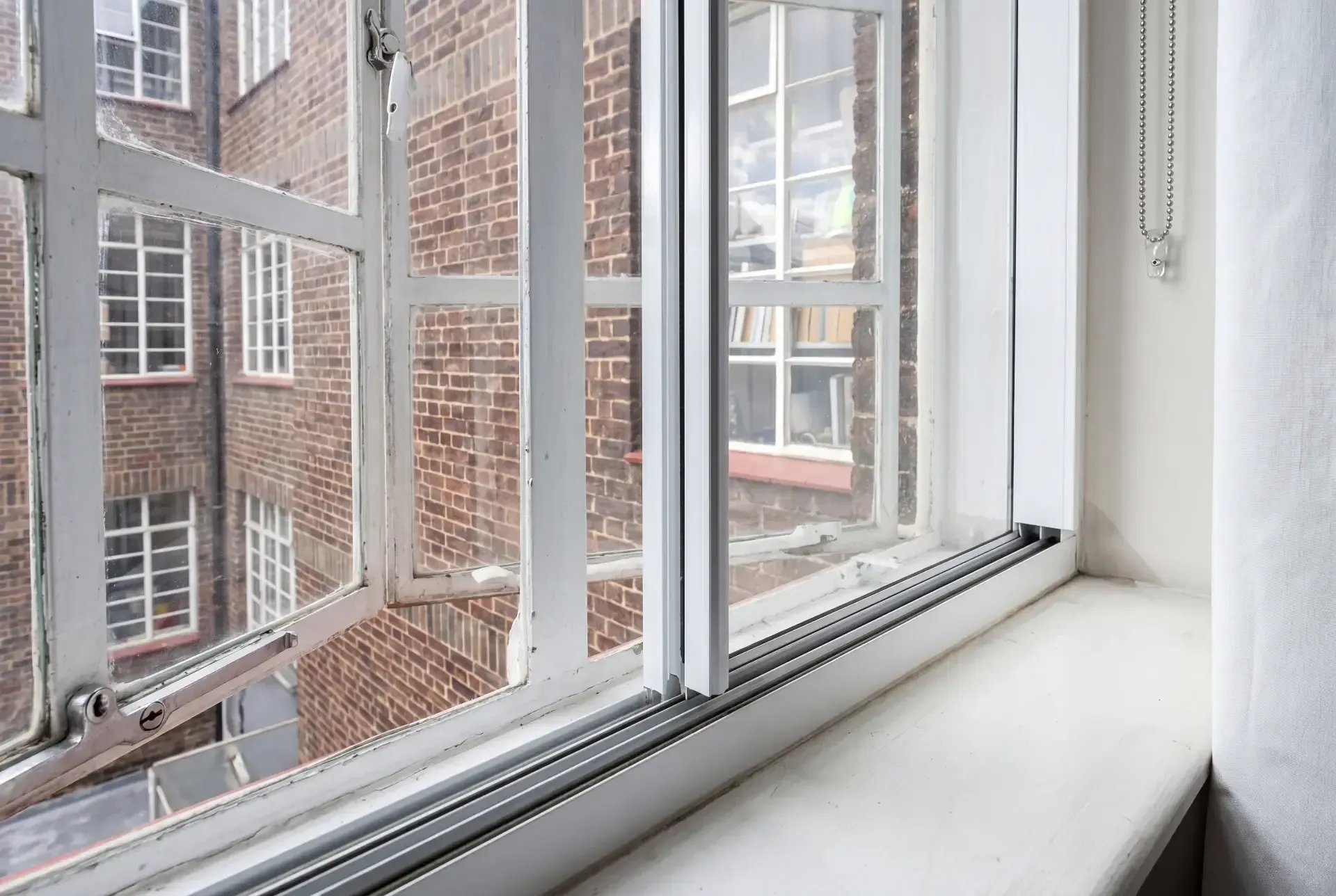 Close-up of a slimline secondary glazing track and frame fitted beside an original single-glazed steel window