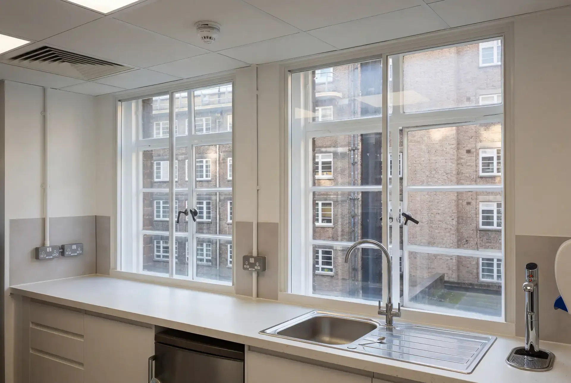 Office kitchen with two tall multi-pane windows fitted with secondary glazing overlooking a brick light well